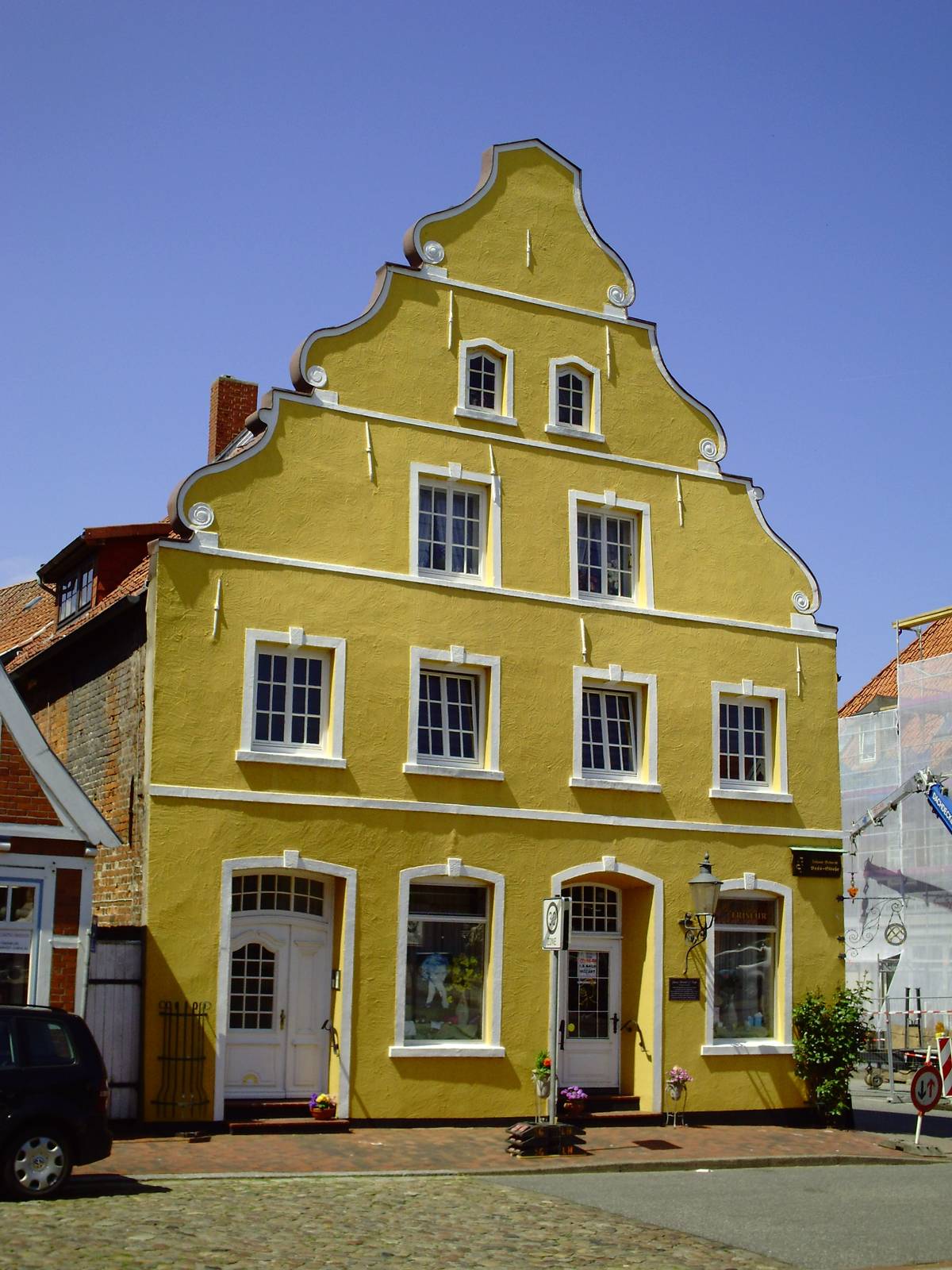 Yellow baroque gabled house with stepped gable and white window frames in Otterndorf's old town, shopfronts on the ground floor