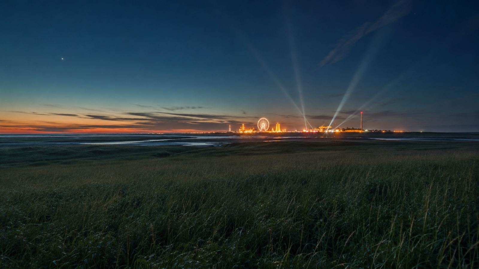 Festival site glowing on the horizon in the evening across the wide North Sea coastal landscape