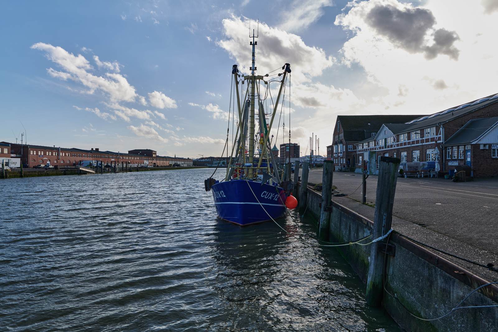 Old fishing harbour in Cuxhaven with a fishing cutter at the quay and the historic fish halls behind it