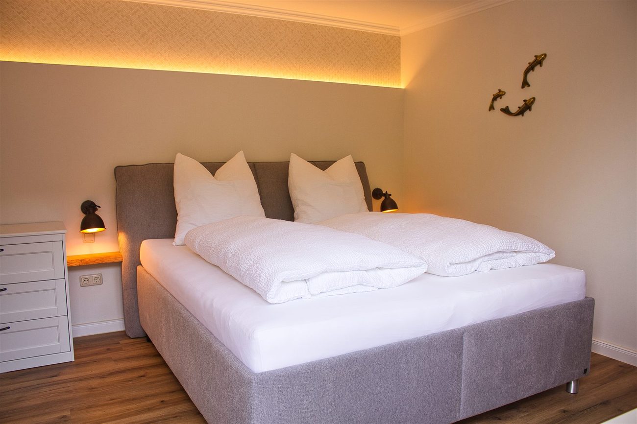 Double bed with a grey upholstered headboard in the Koi room, warm wall lighting, a dresser and fish-shaped wall decorations