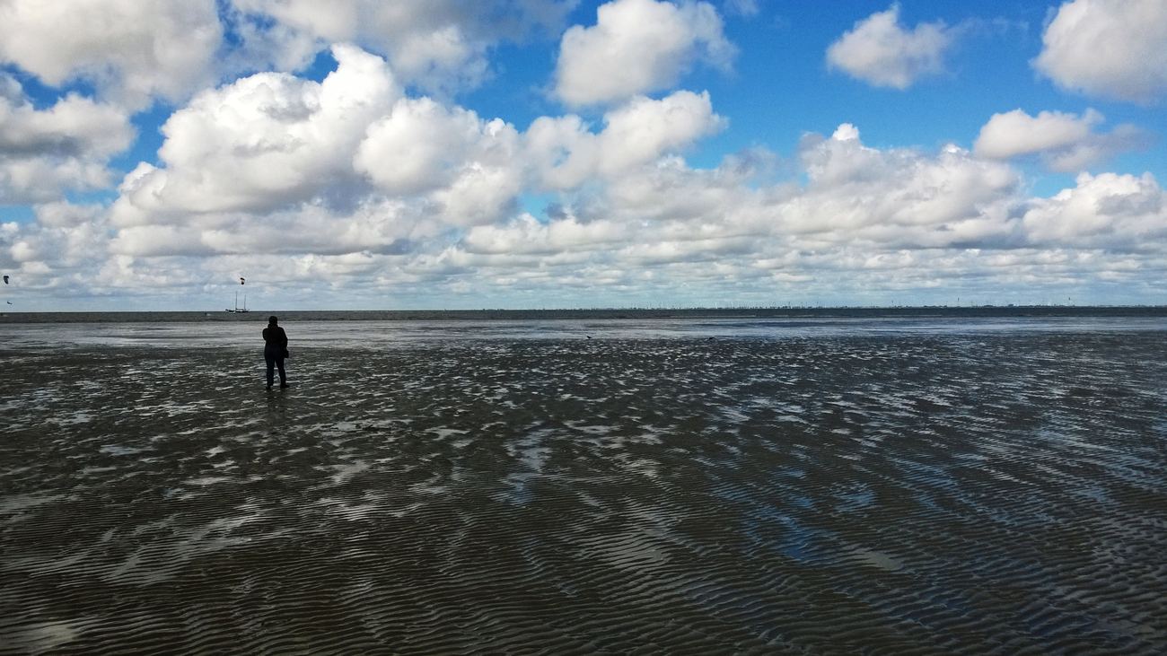 Single person on wide, wet-glistening mudflats at the Elbe beach near Otterndorf, with the horizon line under a large cloudy sky in the background