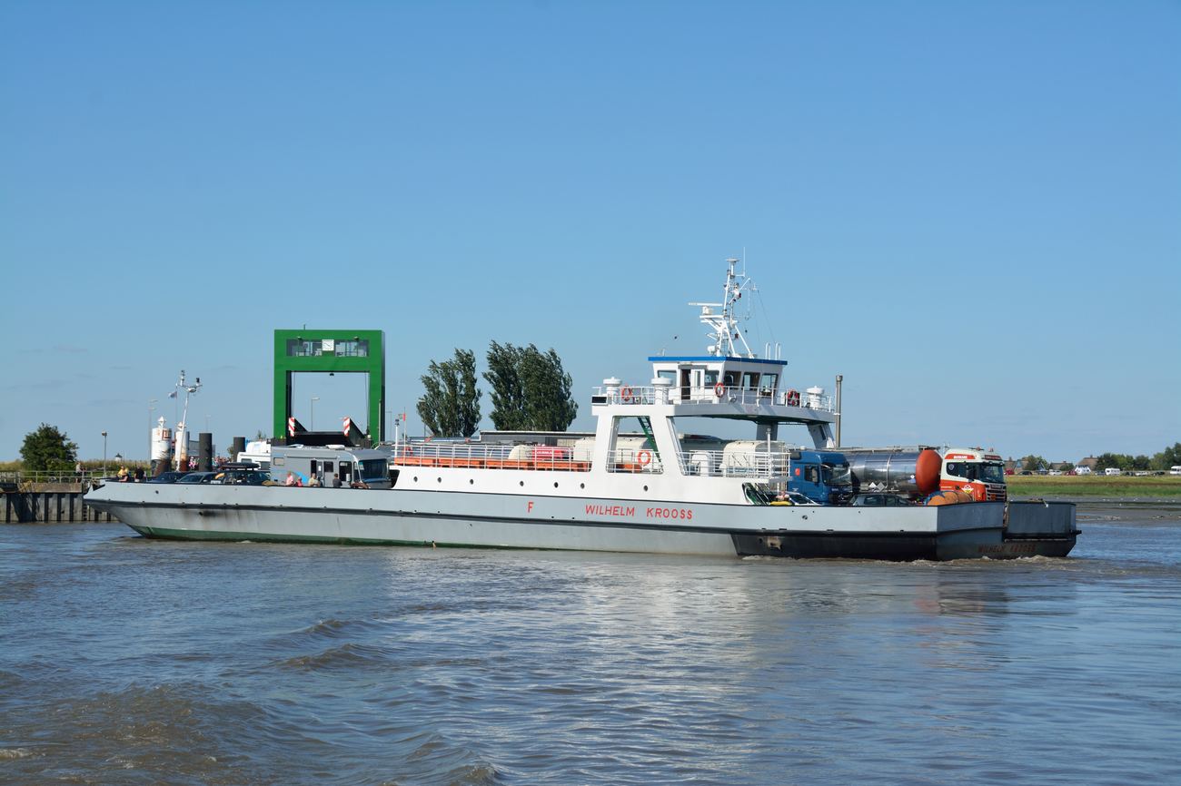 Autofähre Wilhelm Krooss mit Tank-Lkw und Pkw an Bord auf der Elbe, im Hintergrund die grüne Auffahrtrampe am Anleger