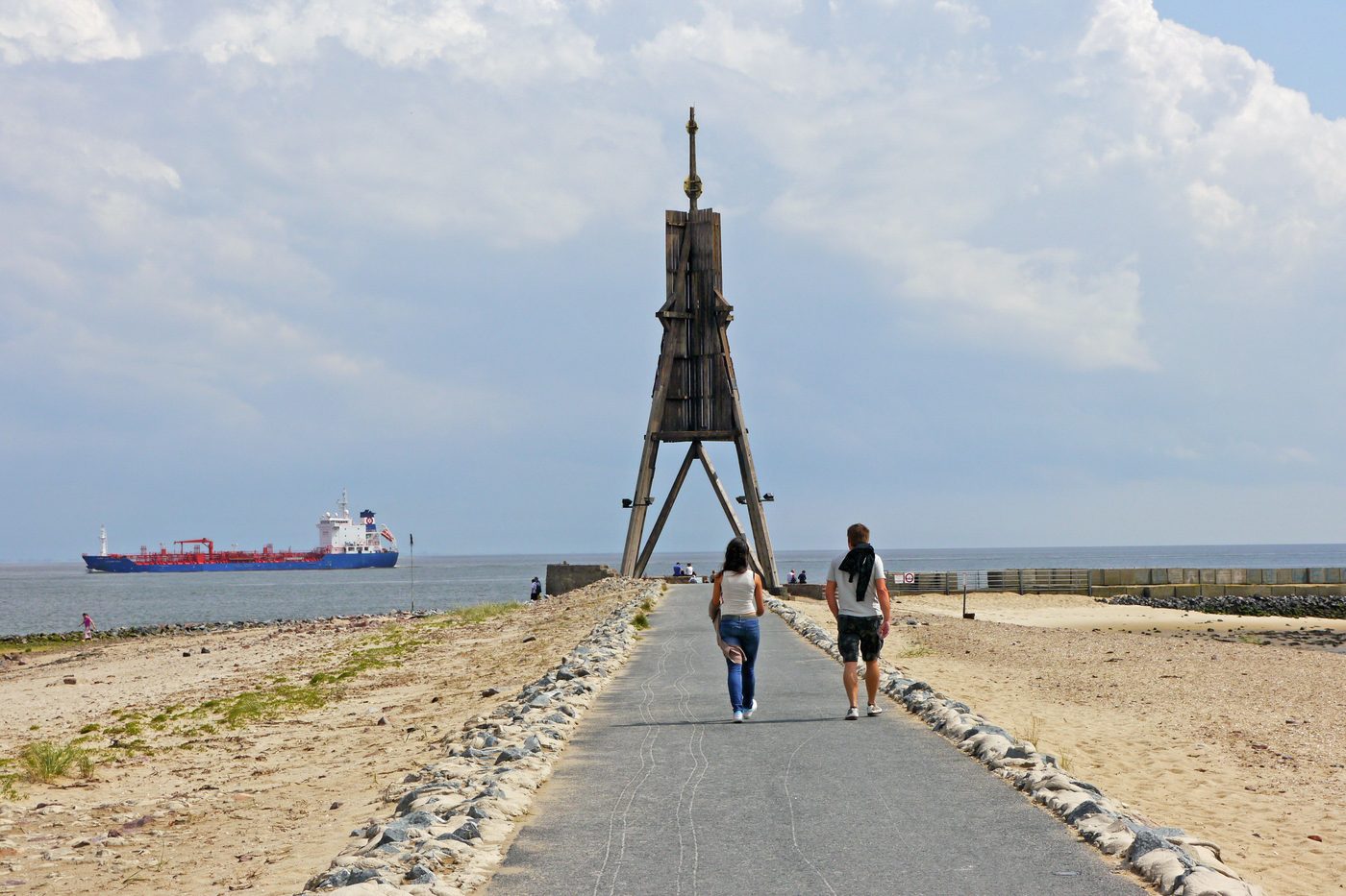 The Kugelbake in Cuxhaven, a wooden navigation mark on the beach, with a footpath and a cargo ship on the water